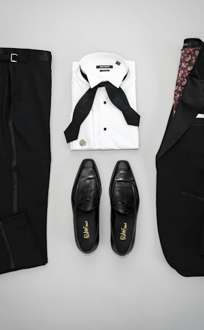 A neatly arranged flat lay of a suit, tie, and leather shoes on a wooden surface.