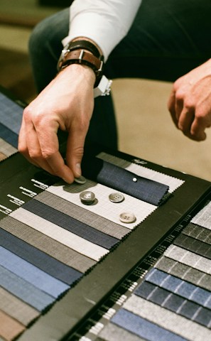 Hands selecting soft, high-quality fabric swatches in warm, neutral tones.