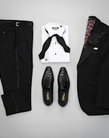 A neatly arranged flat lay of a suit, tie, and leather shoes on a wooden surface.